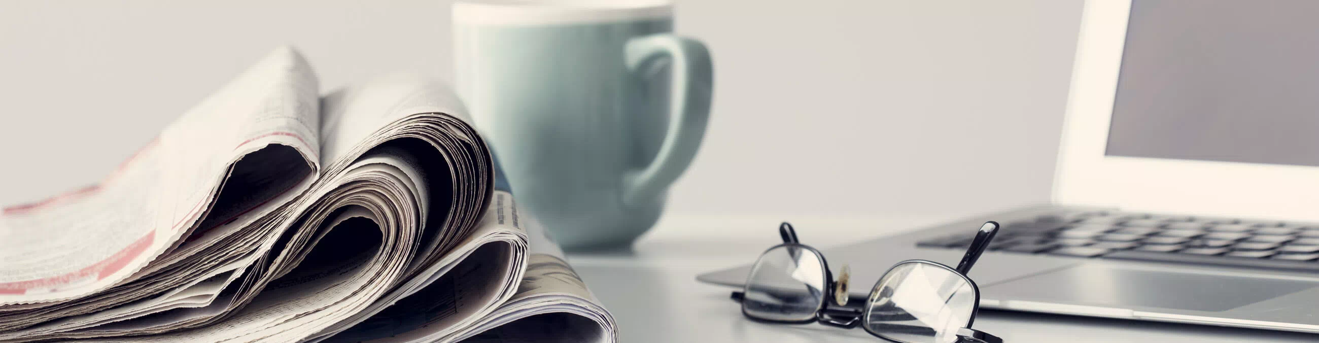 newspapers, reading glasses, a pen, and a cup of coffee on a table